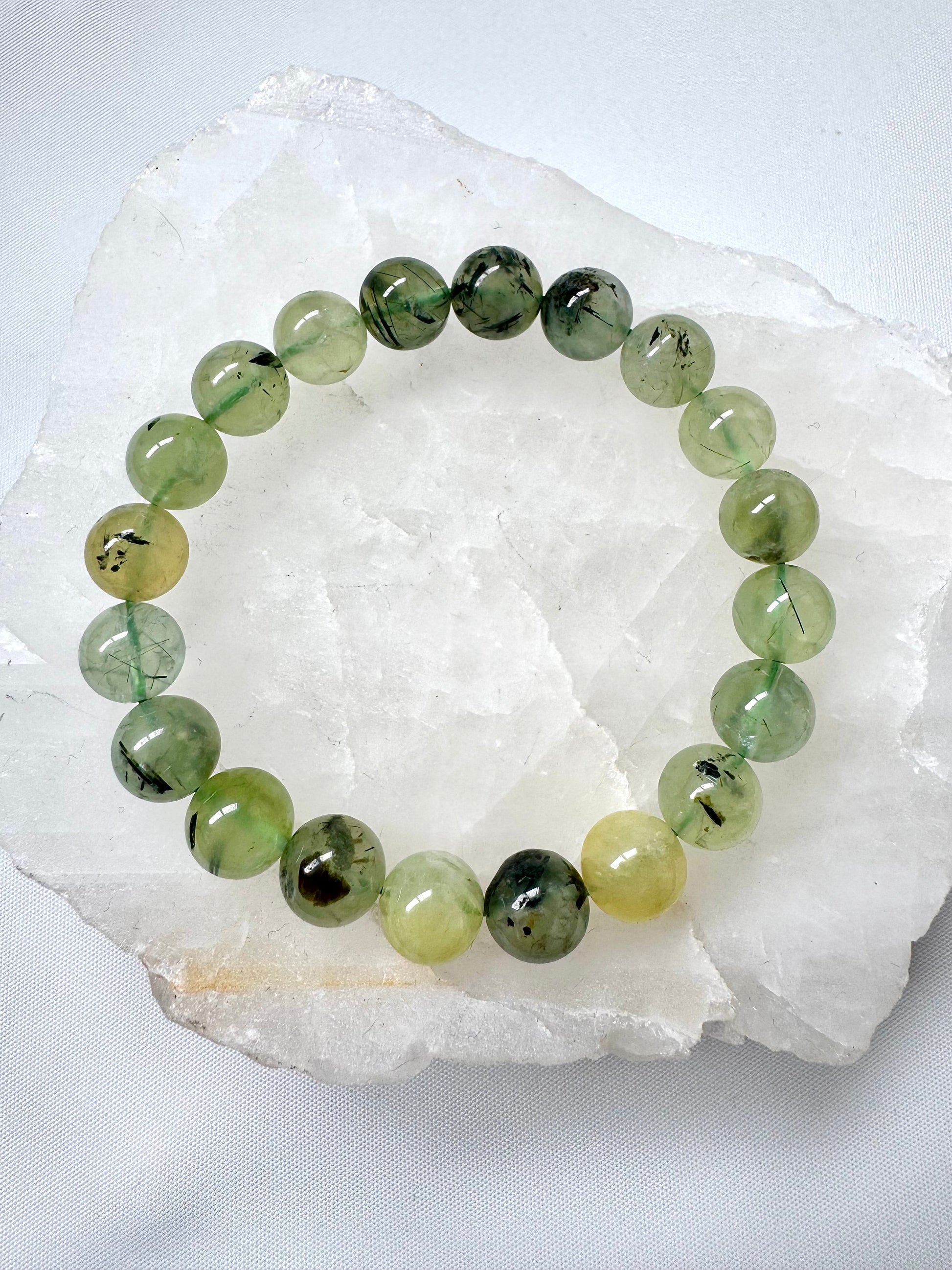 Prehnite Crystal Bracelets 10mm featuring smooth, translucent green beads with epidote inclusions, displayed on a white quartz slab.