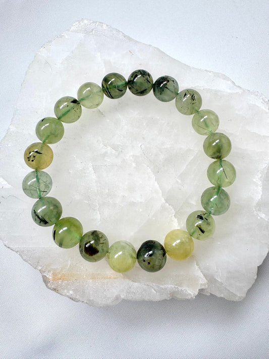 Prehnite Crystal Bracelets 10mm featuring smooth, translucent green beads with epidote inclusions, displayed on a white quartz slab.