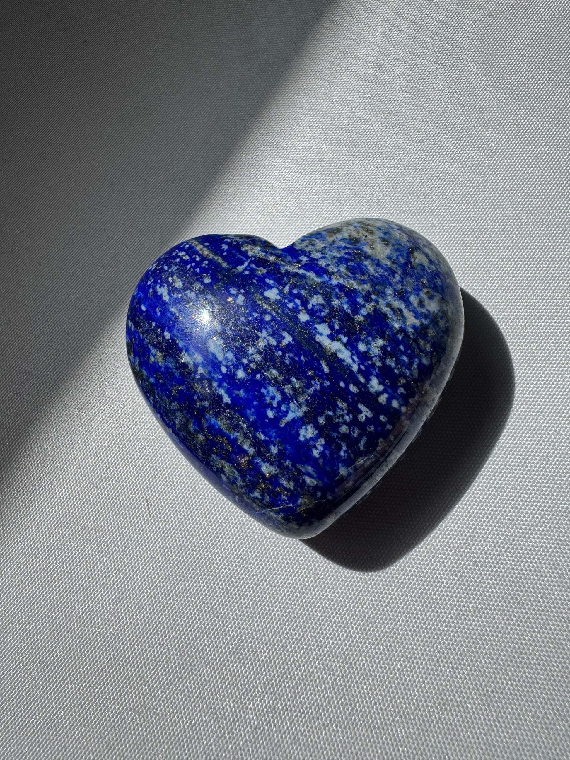 Lapis Lazuli Heart | Bespoke Crystals gemstone with rich blue coloration and speckled pyrite, lying flat on a softly lit white surface.