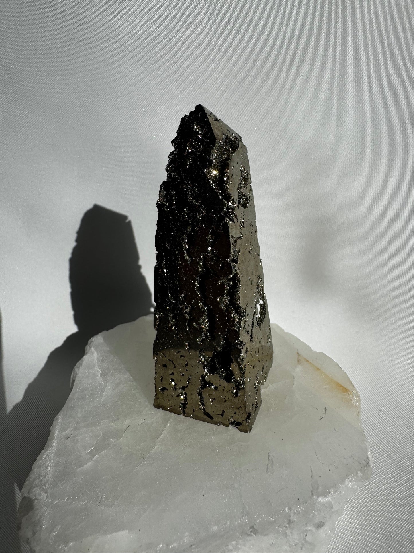 Polished Pyrite Crystal Obelisk #2 standing upright on a translucent white stone, perfect for manifestation and decorative embellishment projects.