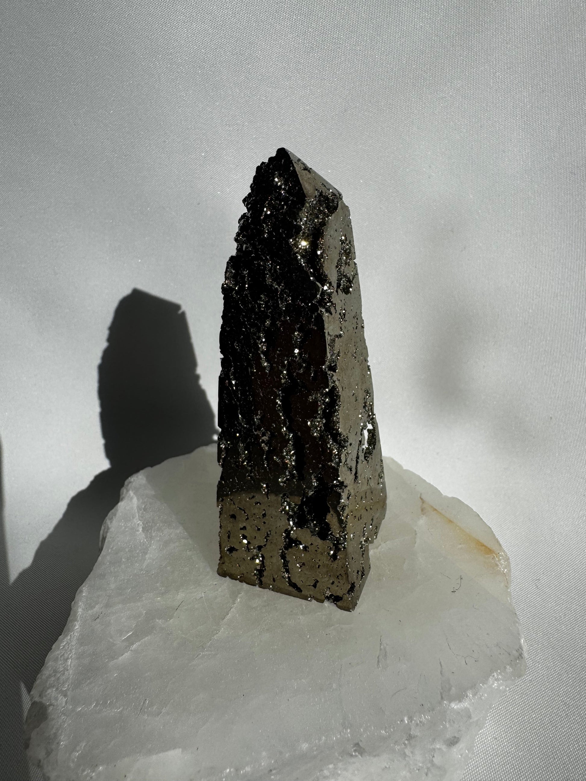 Polished Pyrite Crystal Obelisk #2 standing upright on a translucent white stone, perfect for manifestation and decorative embellishment projects.