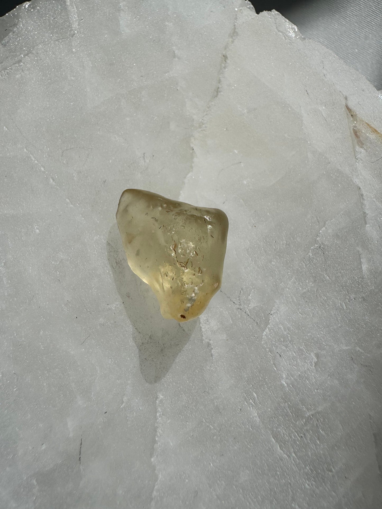 Rare Libyan Desert Crystal Glass with natural inclusions and light-reflective surface, featured on a white stone base for collectible and metaphysical use.