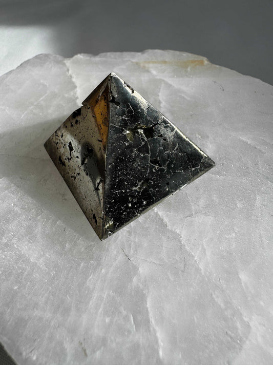 Pyrite Pyramid #14 with a polished metallic finish, displayed on a white crystal slab for wellness and abundance decor or crystal healing collections.