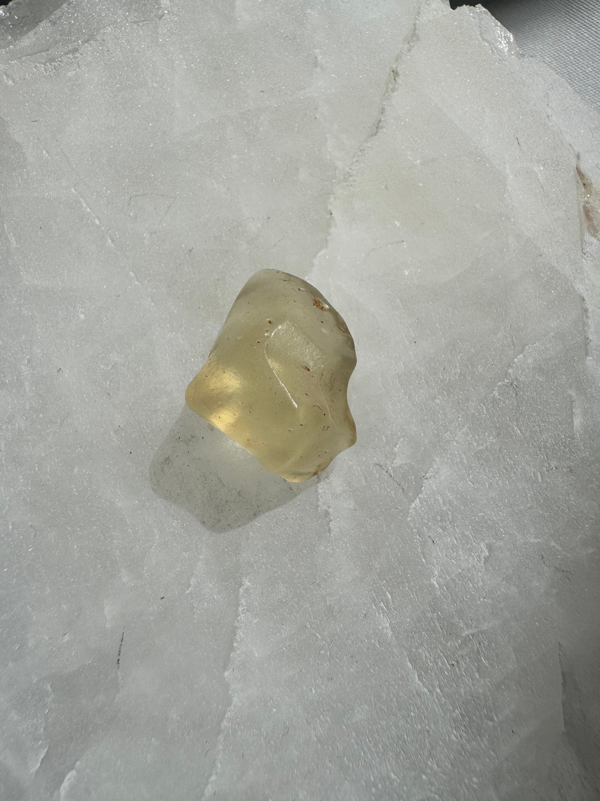 Polished Libyan Desert Crystal Glass specimen showing smooth texture and golden clarity, placed on a white crystal surface for arts and fossil collections.