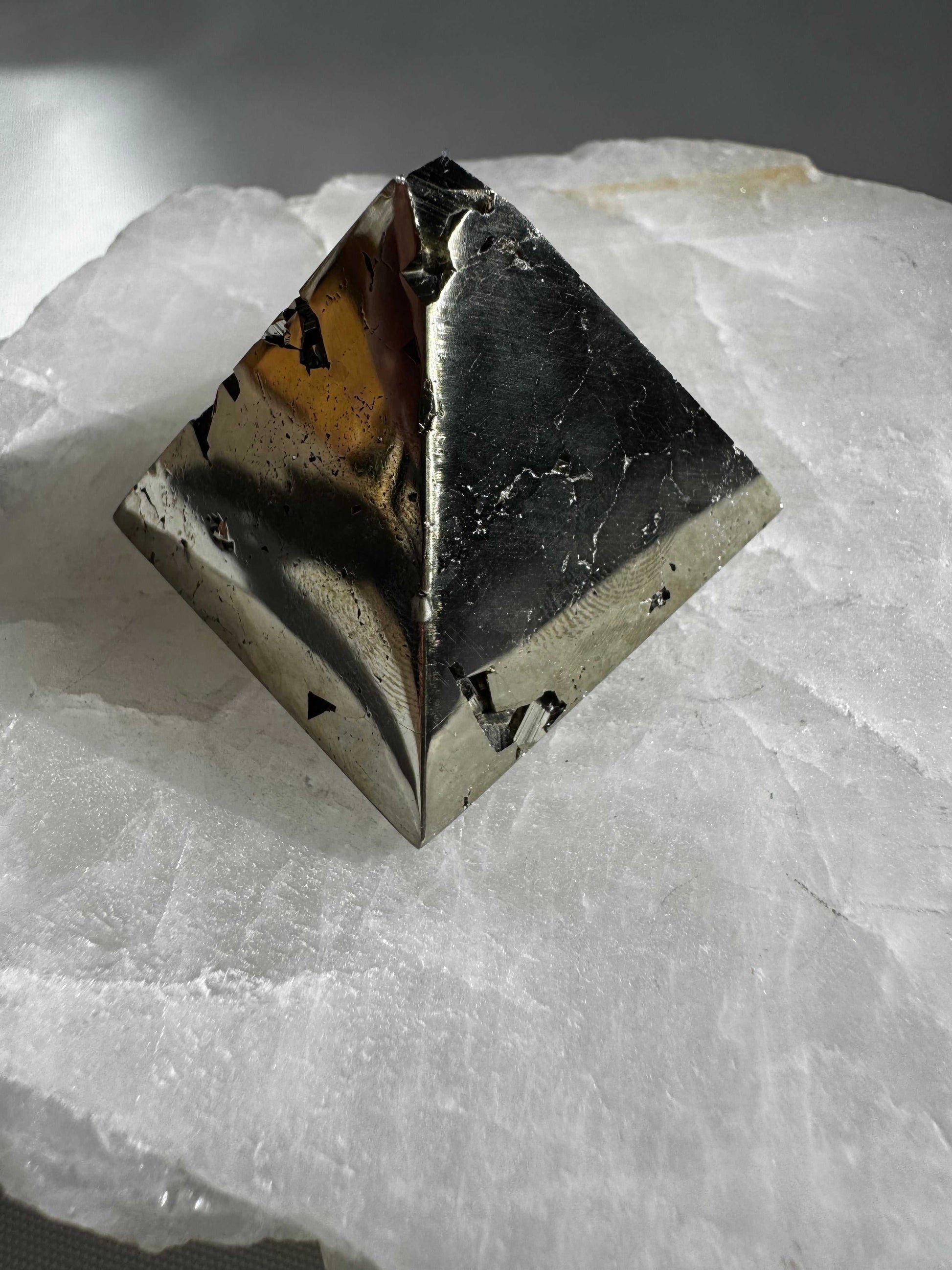 Pyrite Pyramid #2 with metallic luster and natural inclusions, displayed on a white crystal slab for wellness and abundance decor.