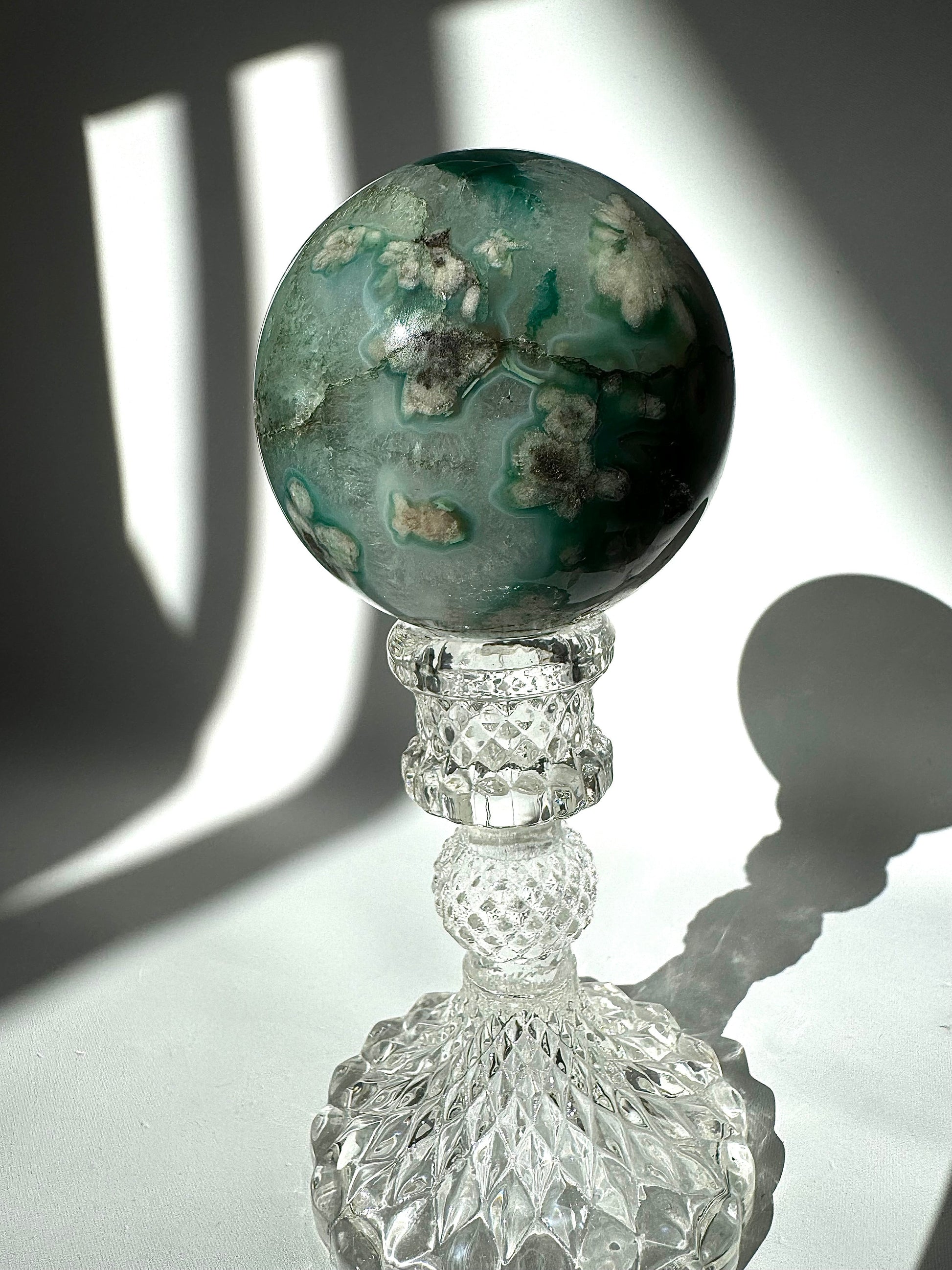 Green Flower Agate Crystal Sphere #1 with intricate white and green inclusions, placed on a vintage-style crystal pedestal under natural light.
