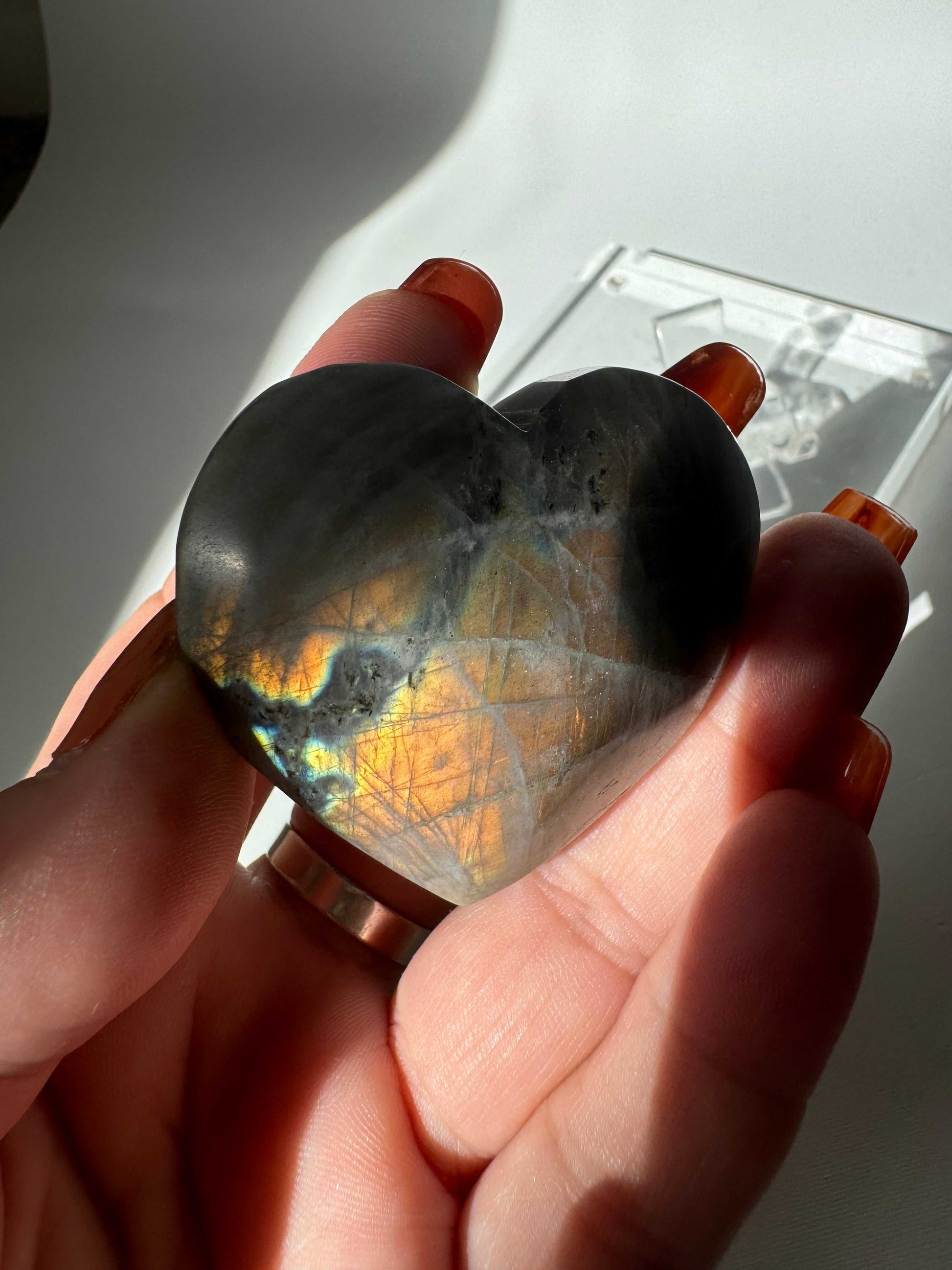 Hand holding Labradorite Puffy Heart #4 with vivid golden and blue flashes, highlighting the crystal's natural labradorescence and smooth finish.