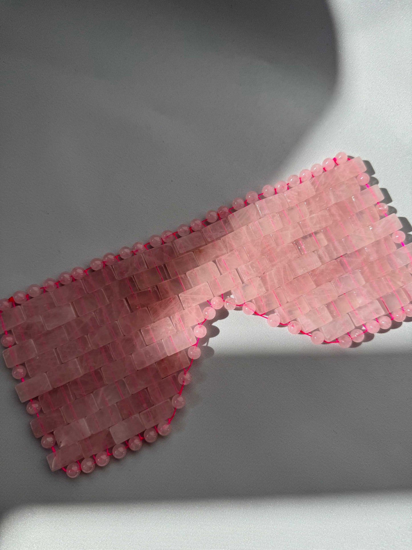 Flat-lay of Rose Quartz Crystal Eye Mask with smooth, polished stones. A luxury sleeping aid for stress relief and calming effects.