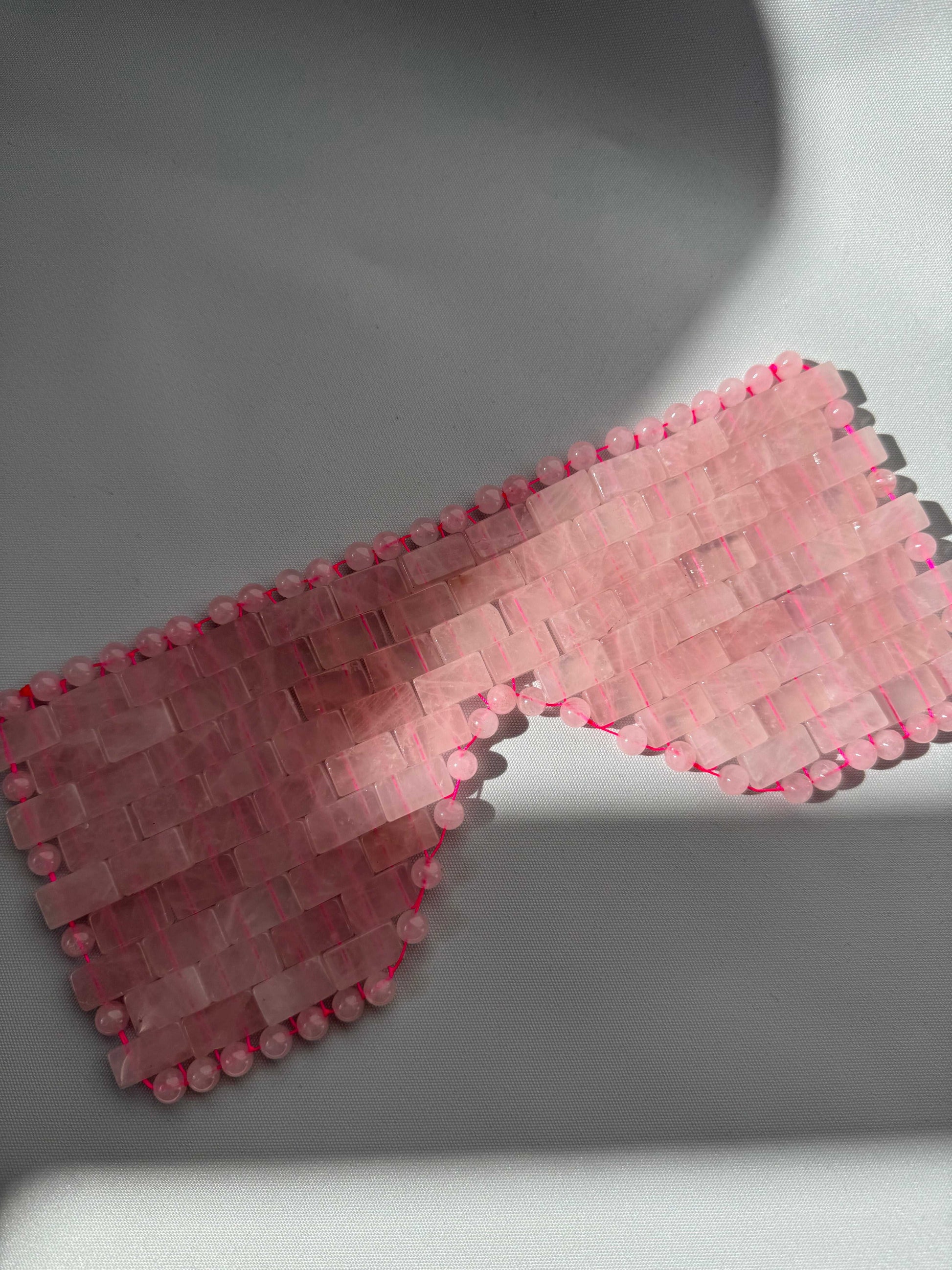 Flat-lay of Rose Quartz Crystal Eye Mask with smooth, polished stones. A luxury sleeping aid for stress relief and calming effects.