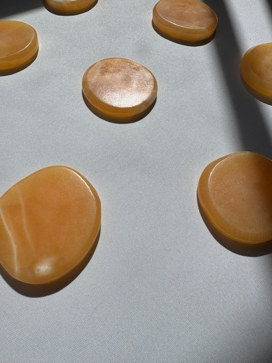 Orange Calcite Crystal Sun Discs | Bespoke Crystals displayed on white fabric, showcasing their smooth, polished finish and warm amber tones.