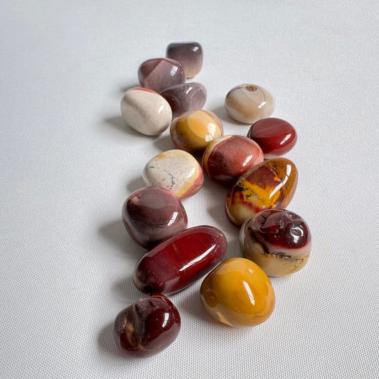 Mookite Tumbler Stones - Grounding Energy Benefits | Crystals NZ. A scattered collection of polished Mookite tumble stones in earthy red, yellow, and cream tones.