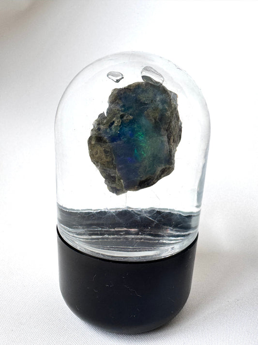 Welo Ethiopian Water Opal in a clear dome display with black base, showcasing vibrant play of color for creativity and emotional healing.