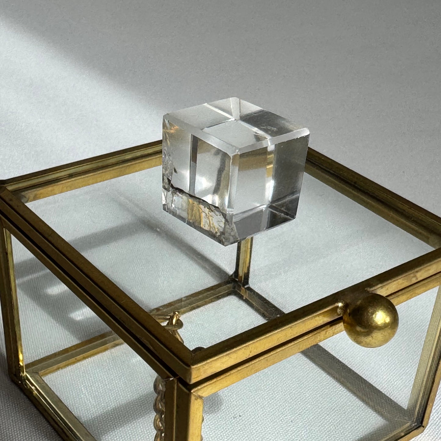Single Lemurian Hexahedron Cube placed on a glass and brass display box, emphasizing its polished finish and geometric precision.