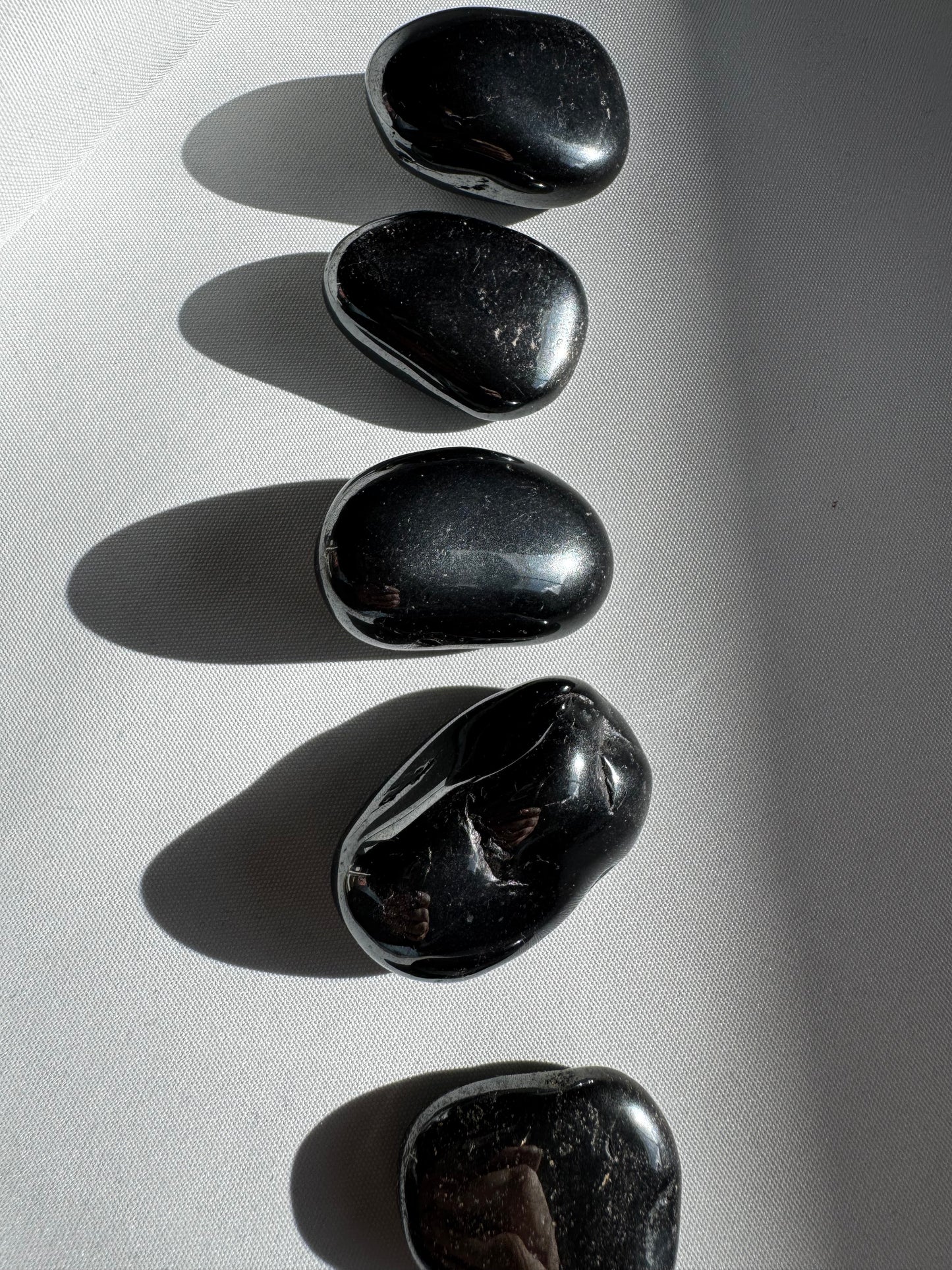 Set of Bespoke Hematite Tumble Stones aligned on a white surface, used for chakra balancing and energy protection rituals.