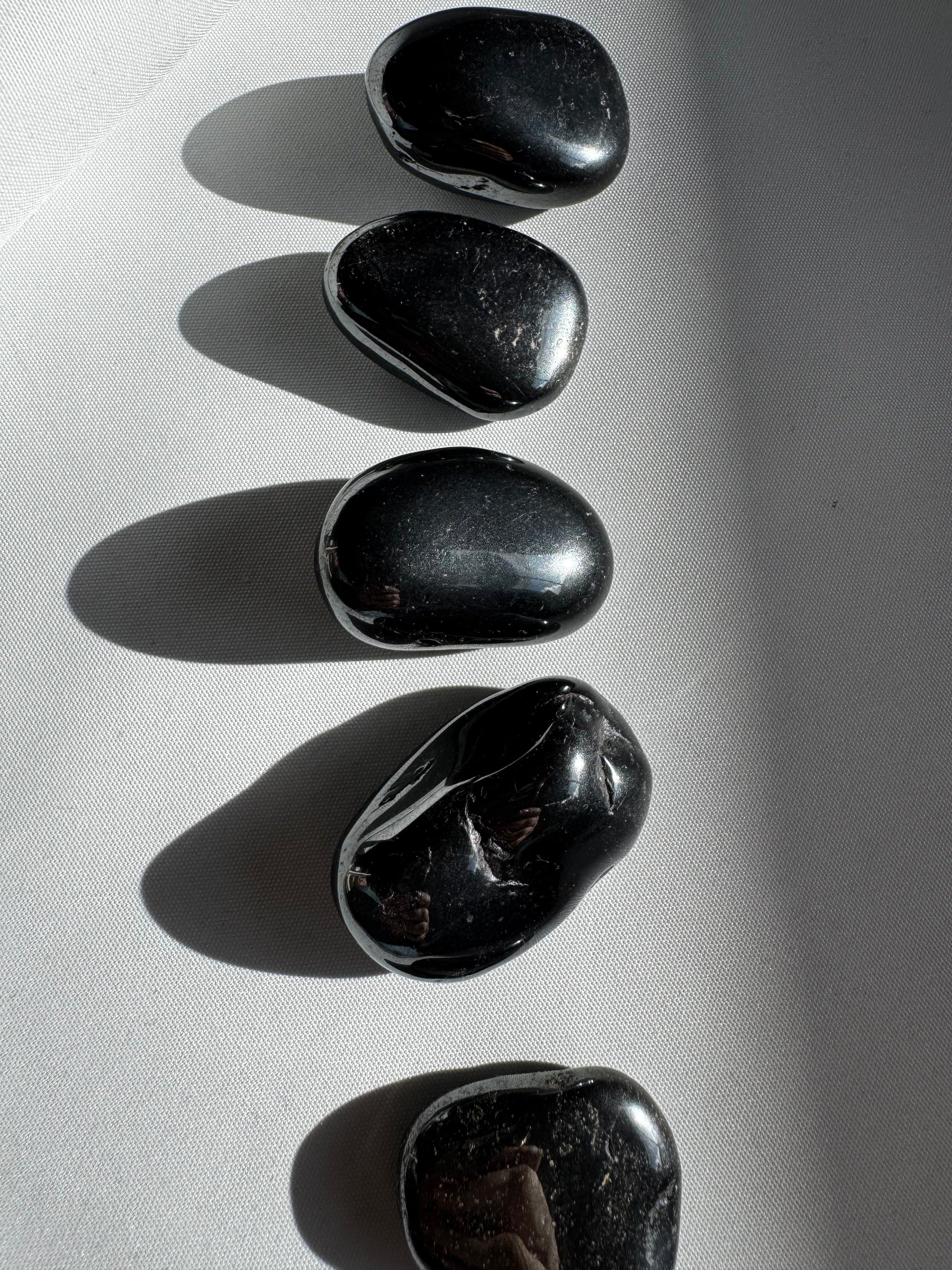 Set of Bespoke Hematite Tumble Stones aligned on a white surface, used for chakra balancing and energy protection rituals.
