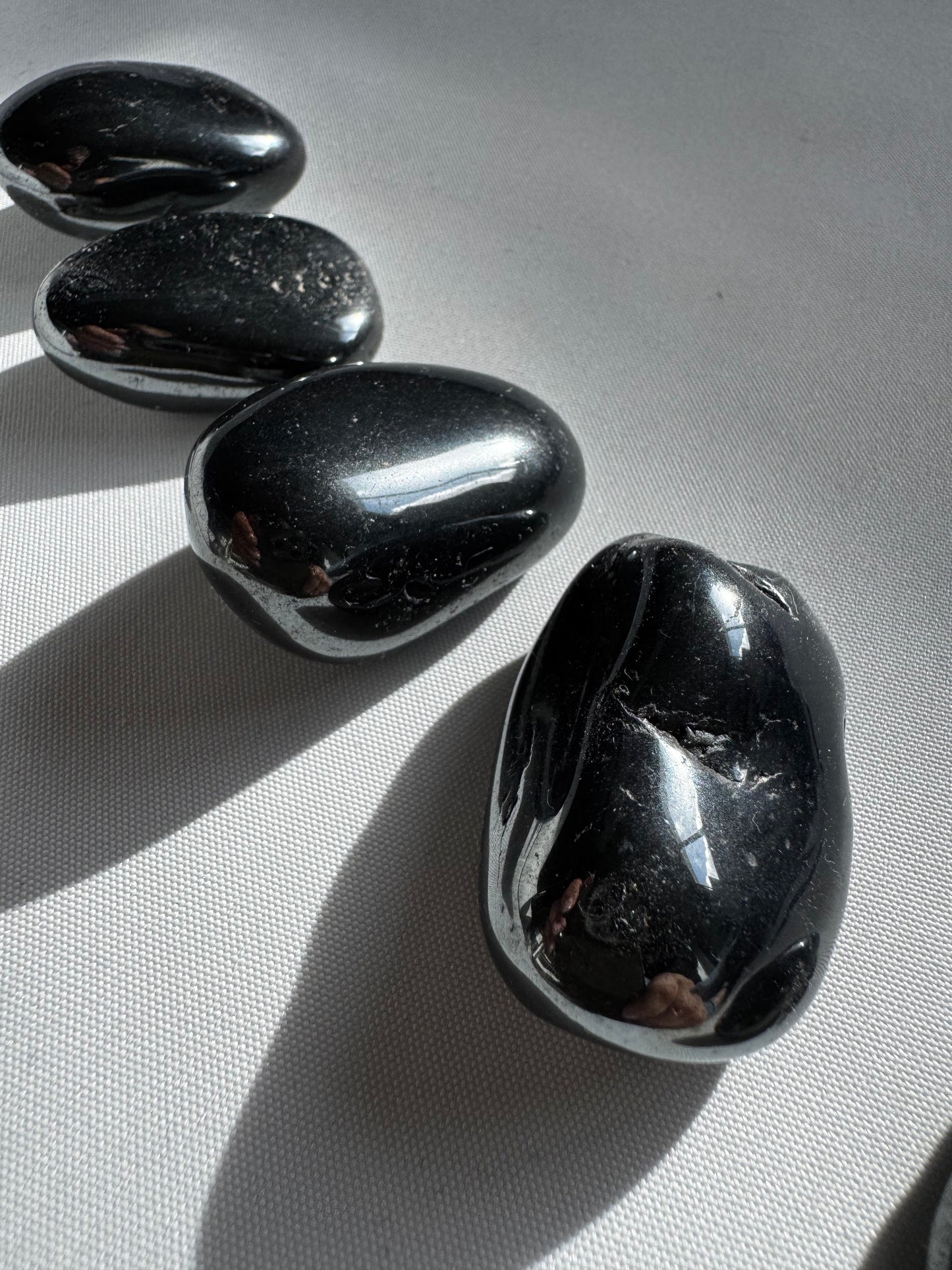 Polished Bespoke Hematite Tumble Stones reflecting light, perfect for protection, mental clarity, and spiritual grounding practices.