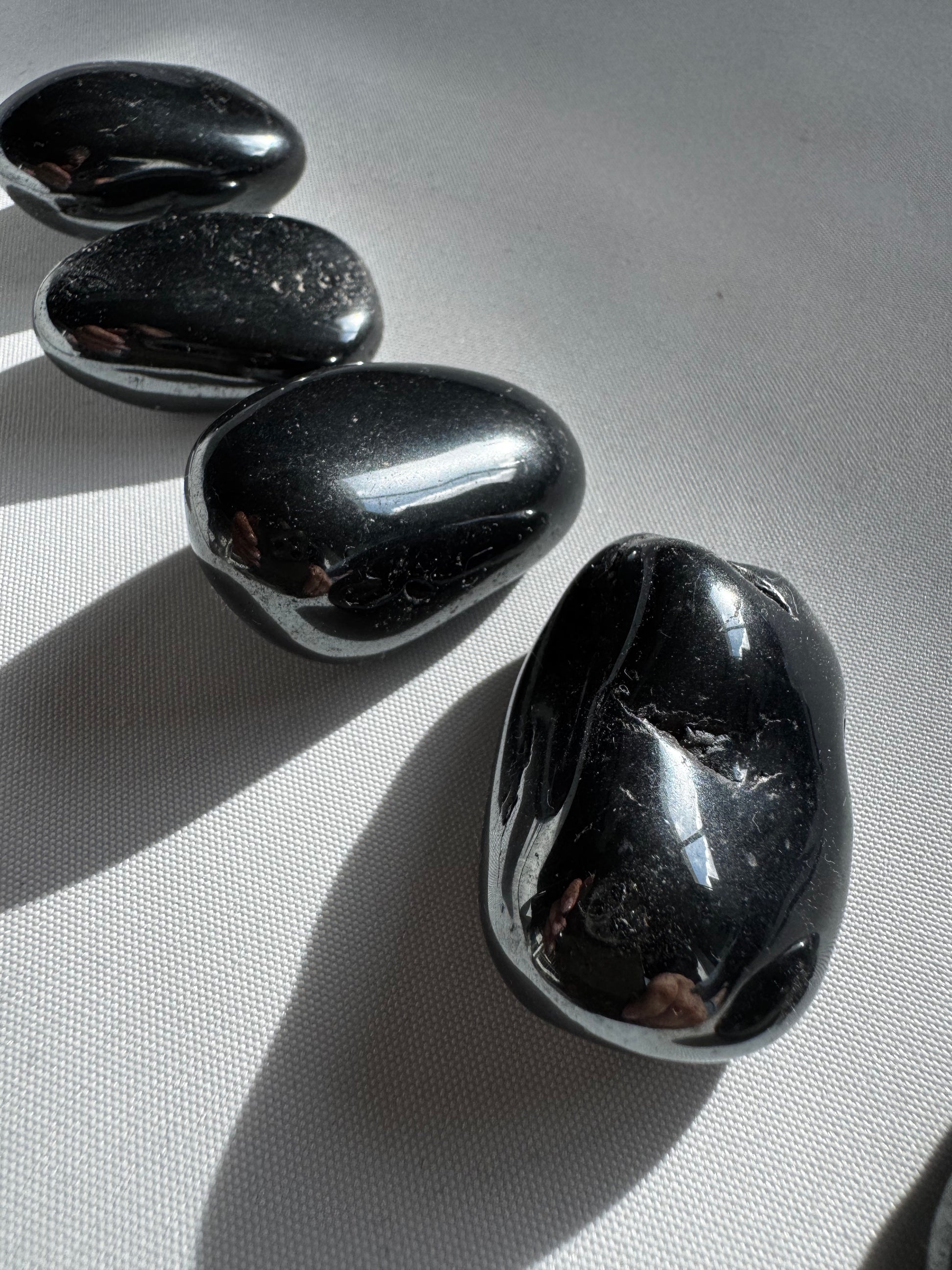 Polished Bespoke Hematite Tumble Stones reflecting light, perfect for protection, mental clarity, and spiritual grounding practices.