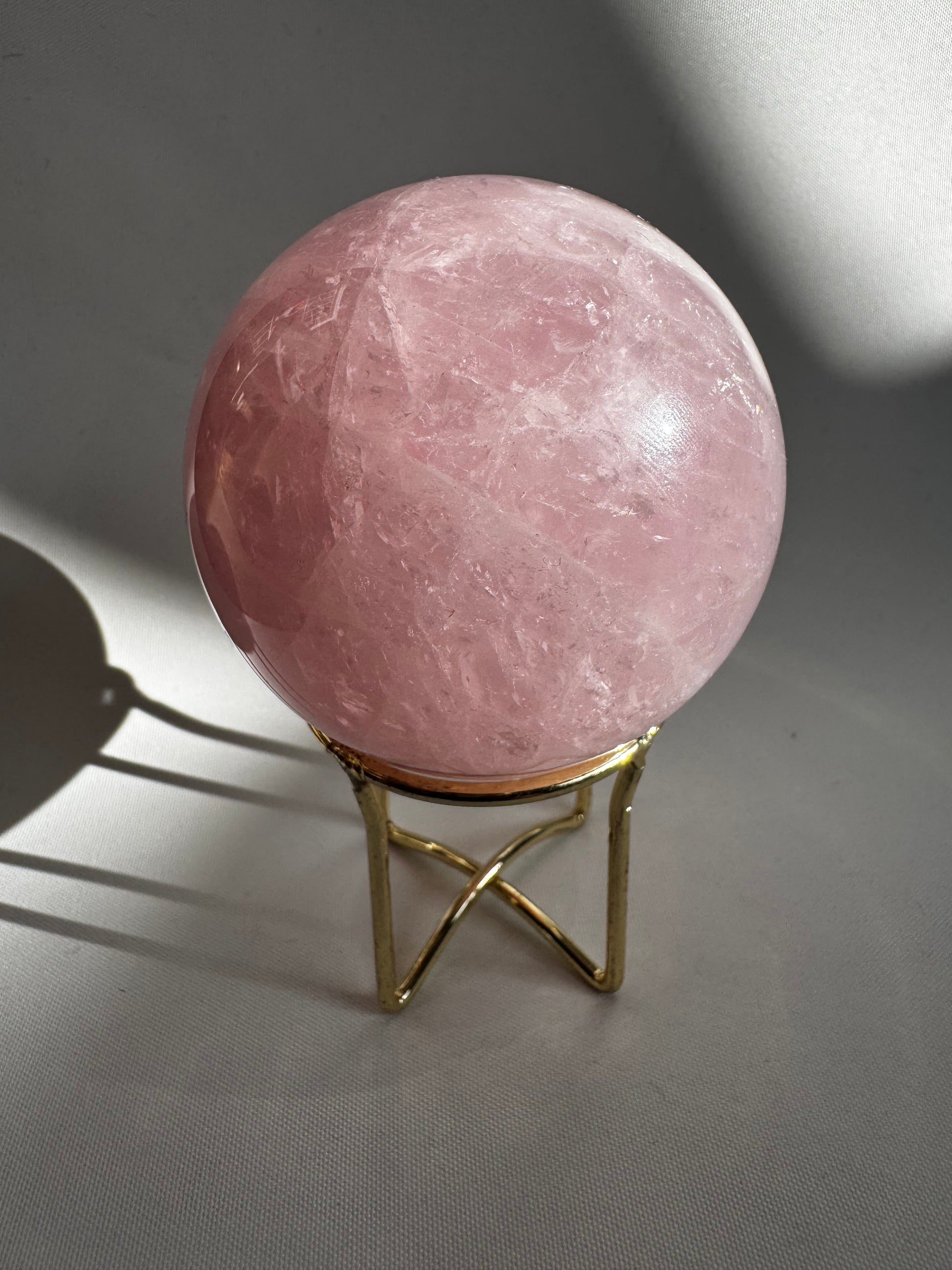 Deep pink Rose Quartz Sphere on metallic gold stand. Shop bespoke crystals online in NZ to enhance your space with calming energy.