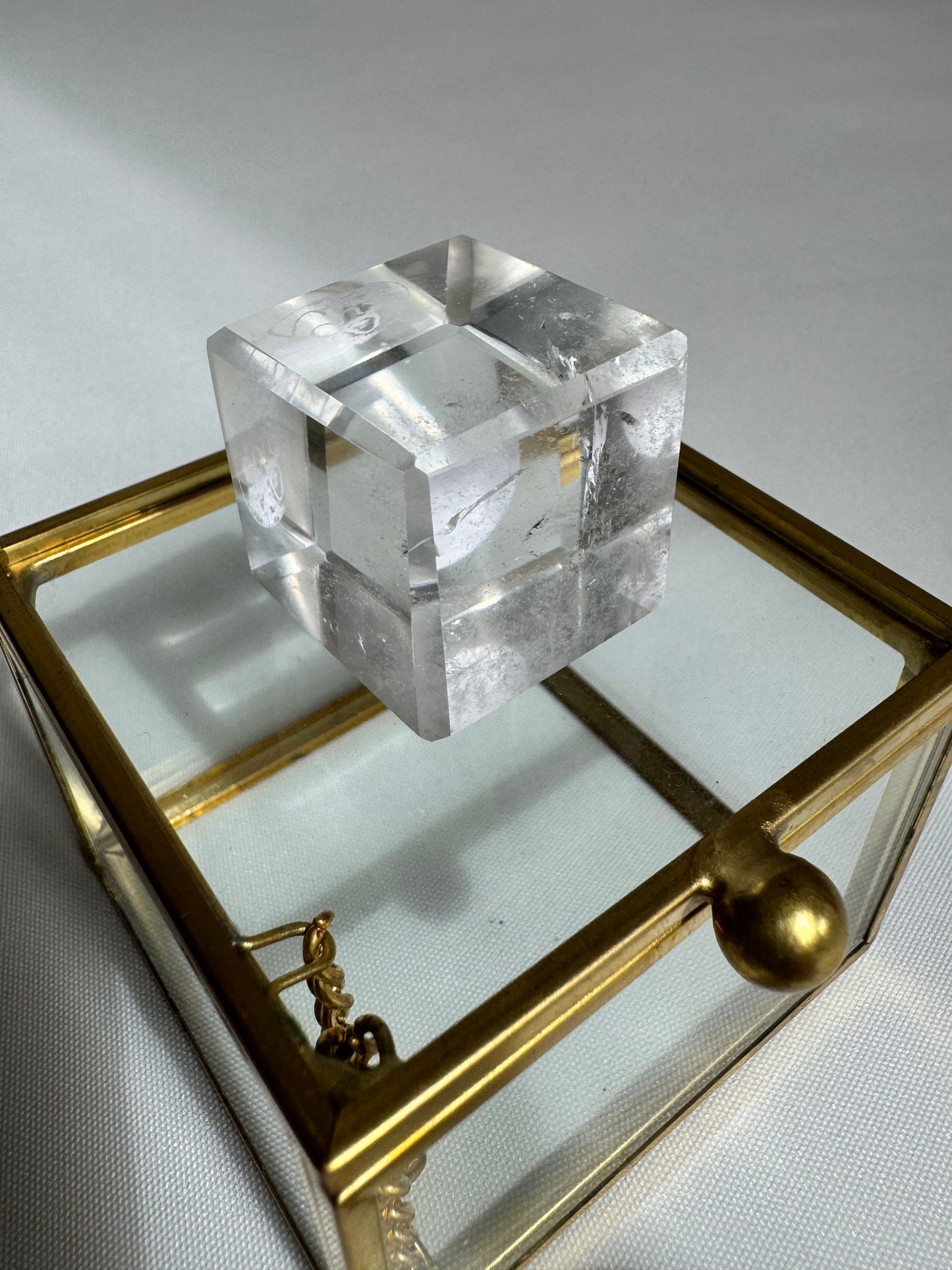 Polished Lemurian Hexahedron Cube resting on a decorative glass box, ideal for meditation and energy work display.