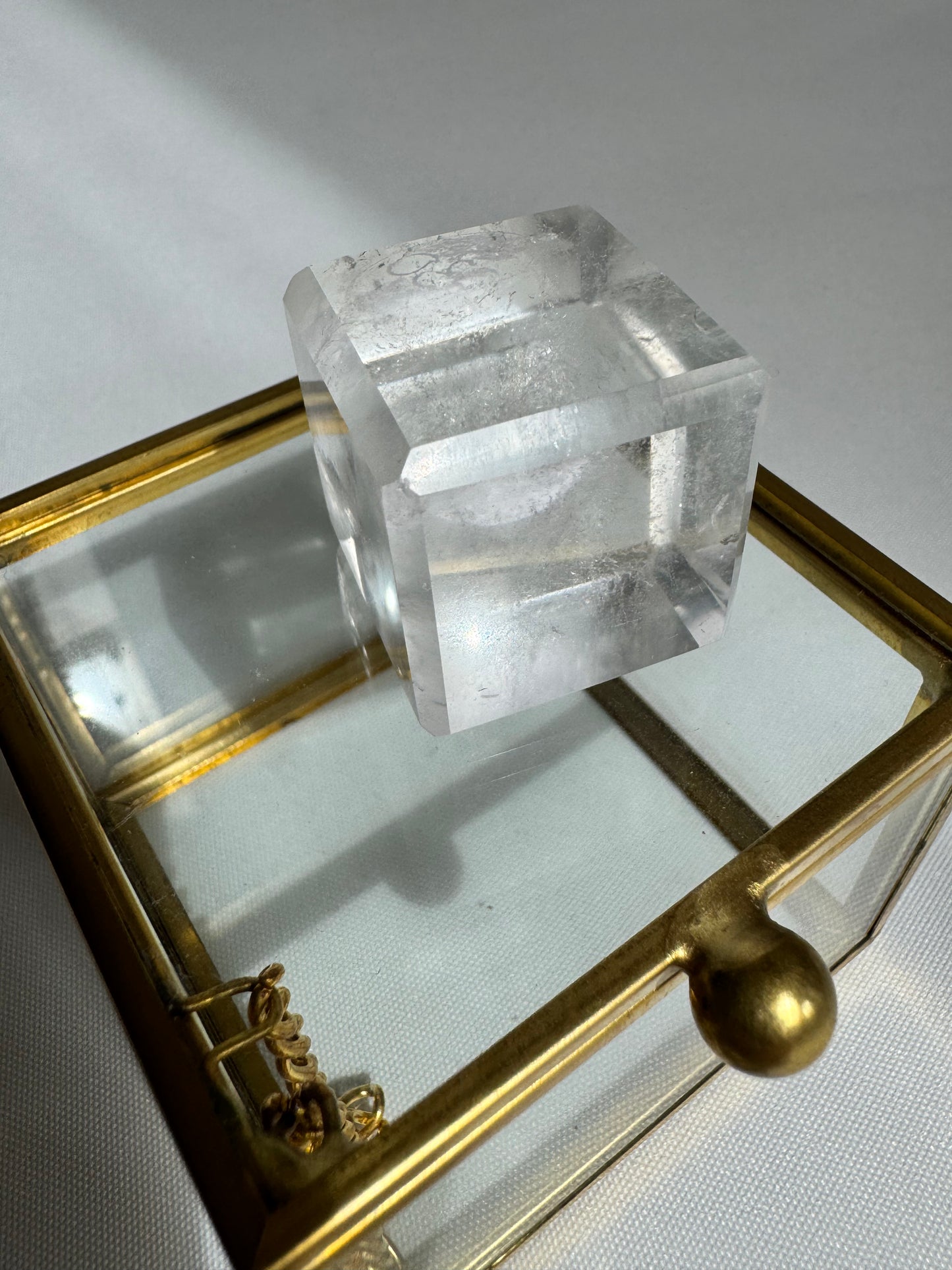 Close-up of a Lemurian Hexahedron Cube on a glass jewelry box, reflecting light to enhance its multidimensional energy appeal.