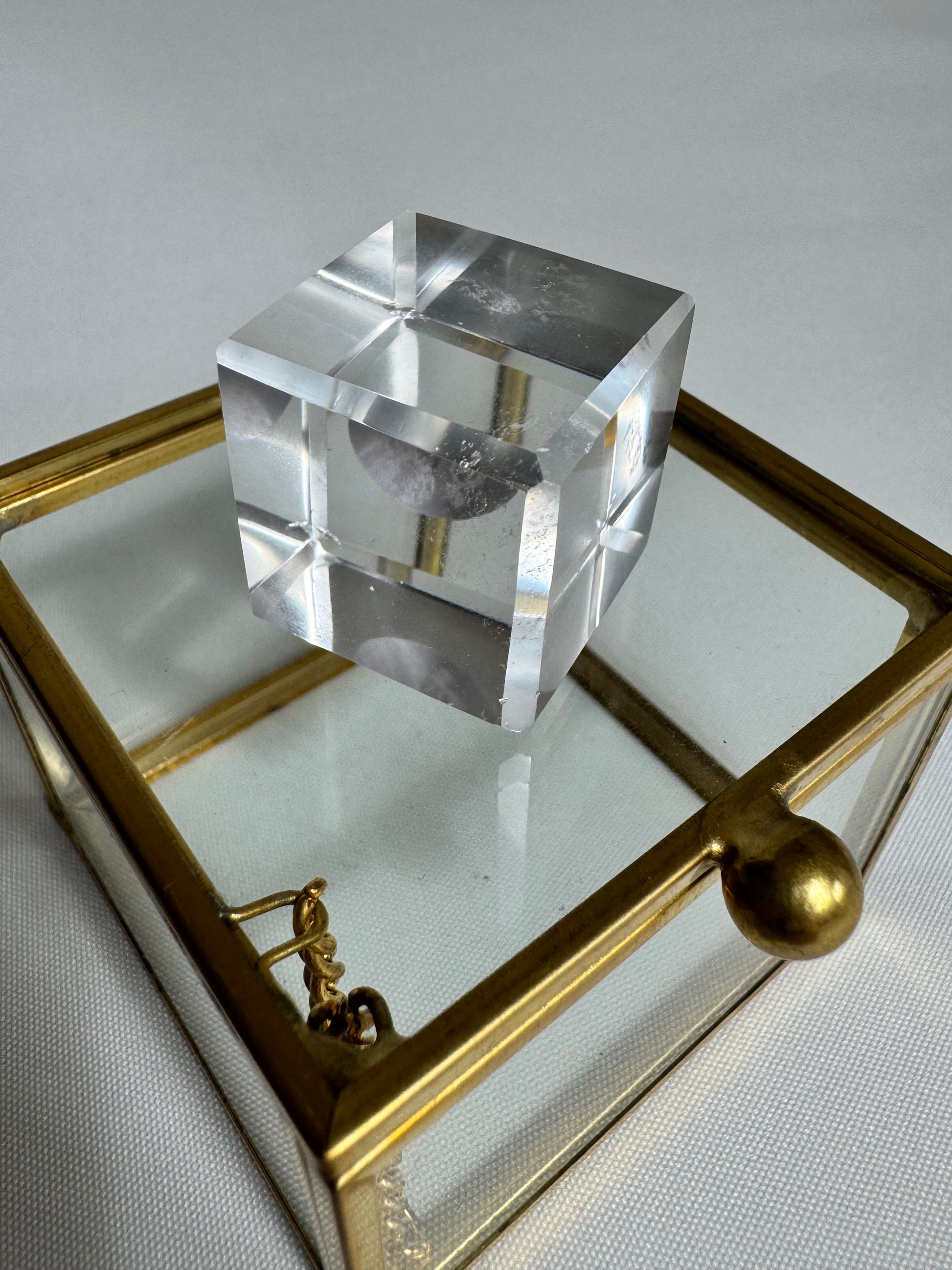 Crystal-clear Lemurian Hexahedron Cube on a glass box, reflecting light to highlight its transformational energy and geometric symmetry.