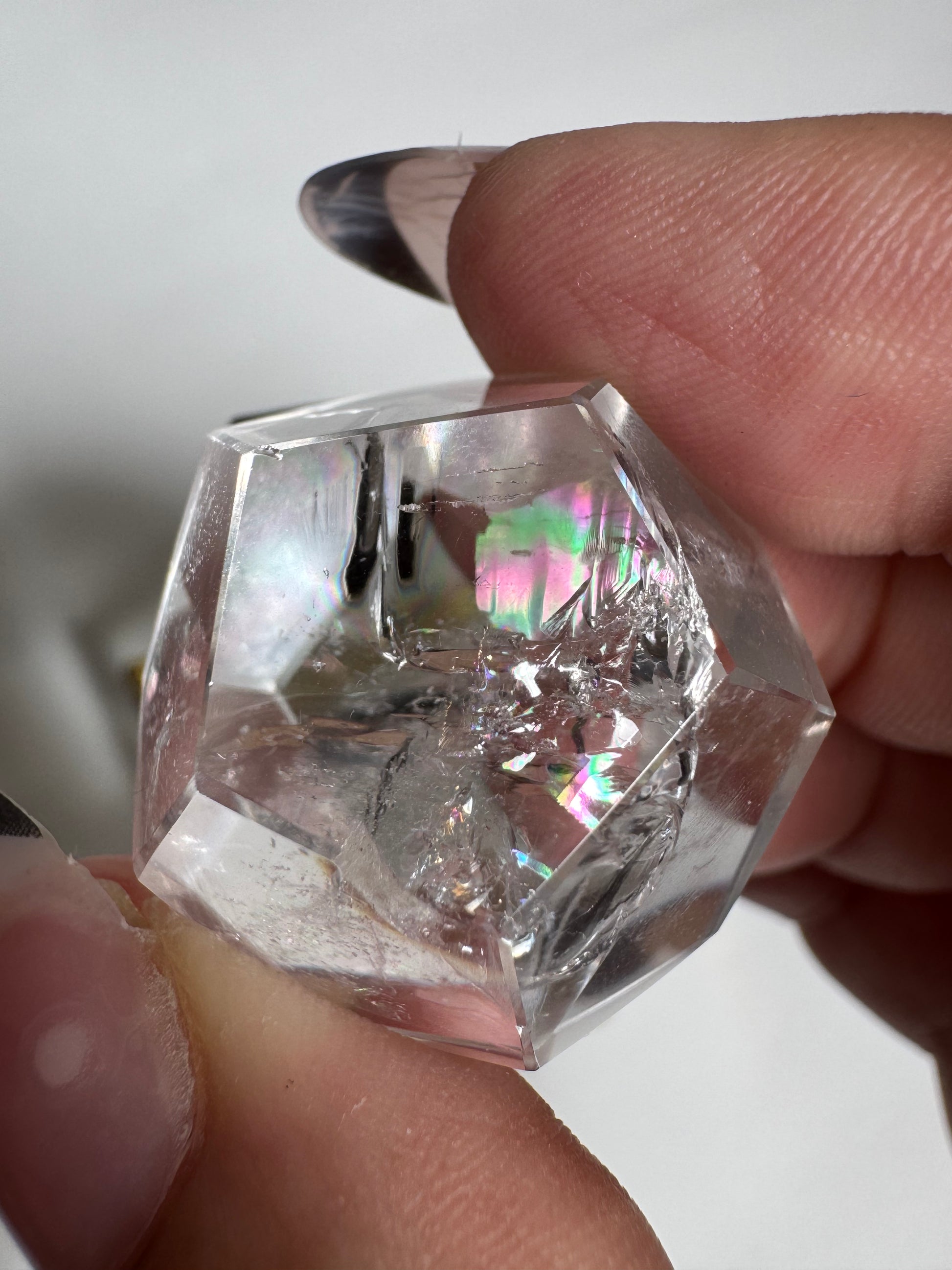 Close-up of Lemurian Quartz Octahedron held between fingers, revealing rainbow inclusions for spiritual growth practices.