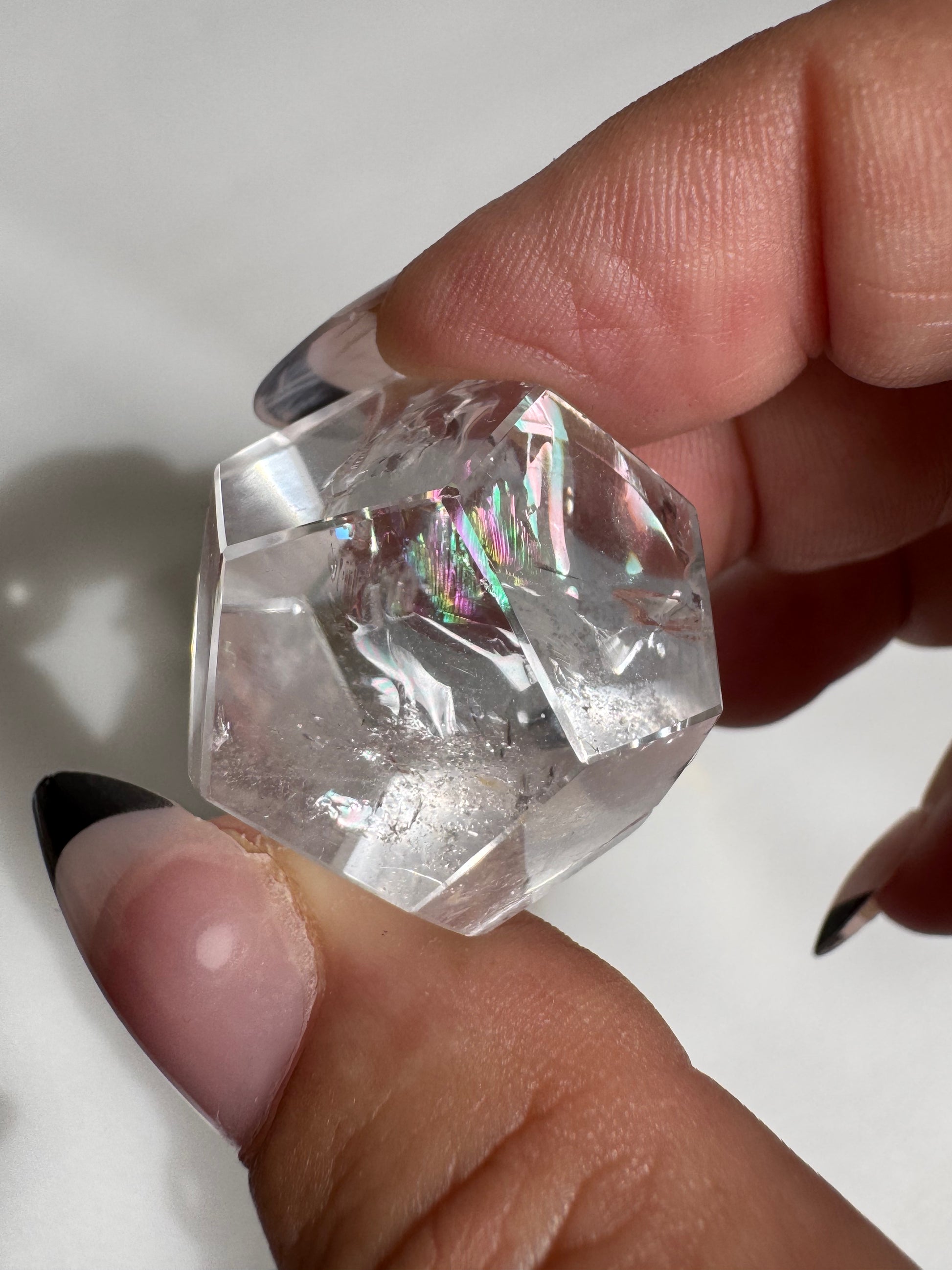 Close-up of a Lemurian Crystal Dodecahedron held between fingers, showcasing internal rainbows and clarity for meditation use.