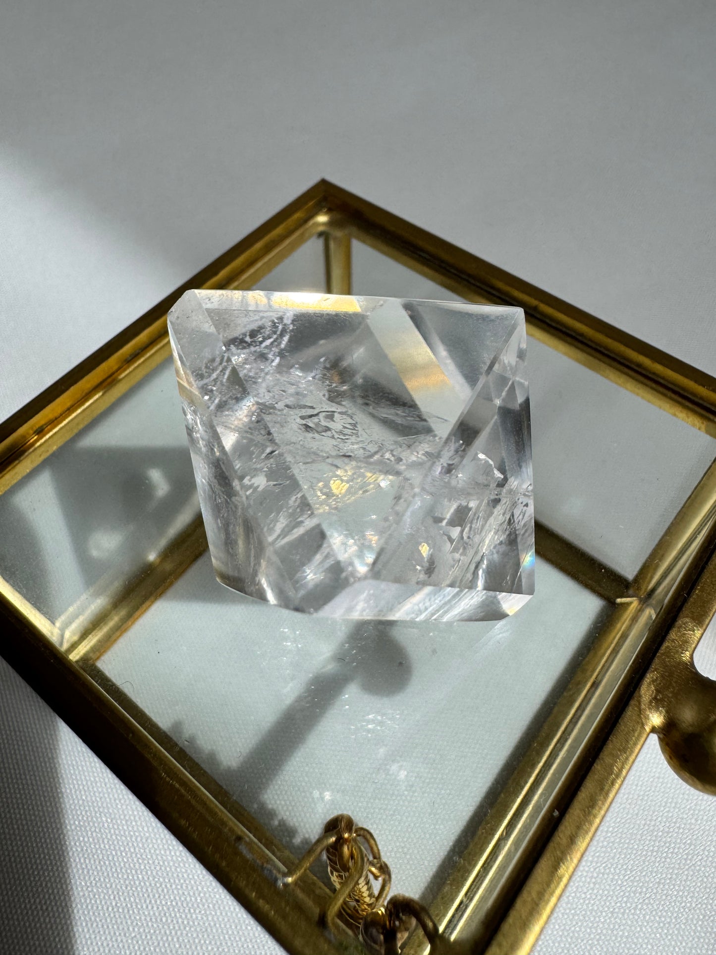 Lemurian Quartz Octahedron resting on glass box, showcasing clarity and internal structure for metaphysical use.