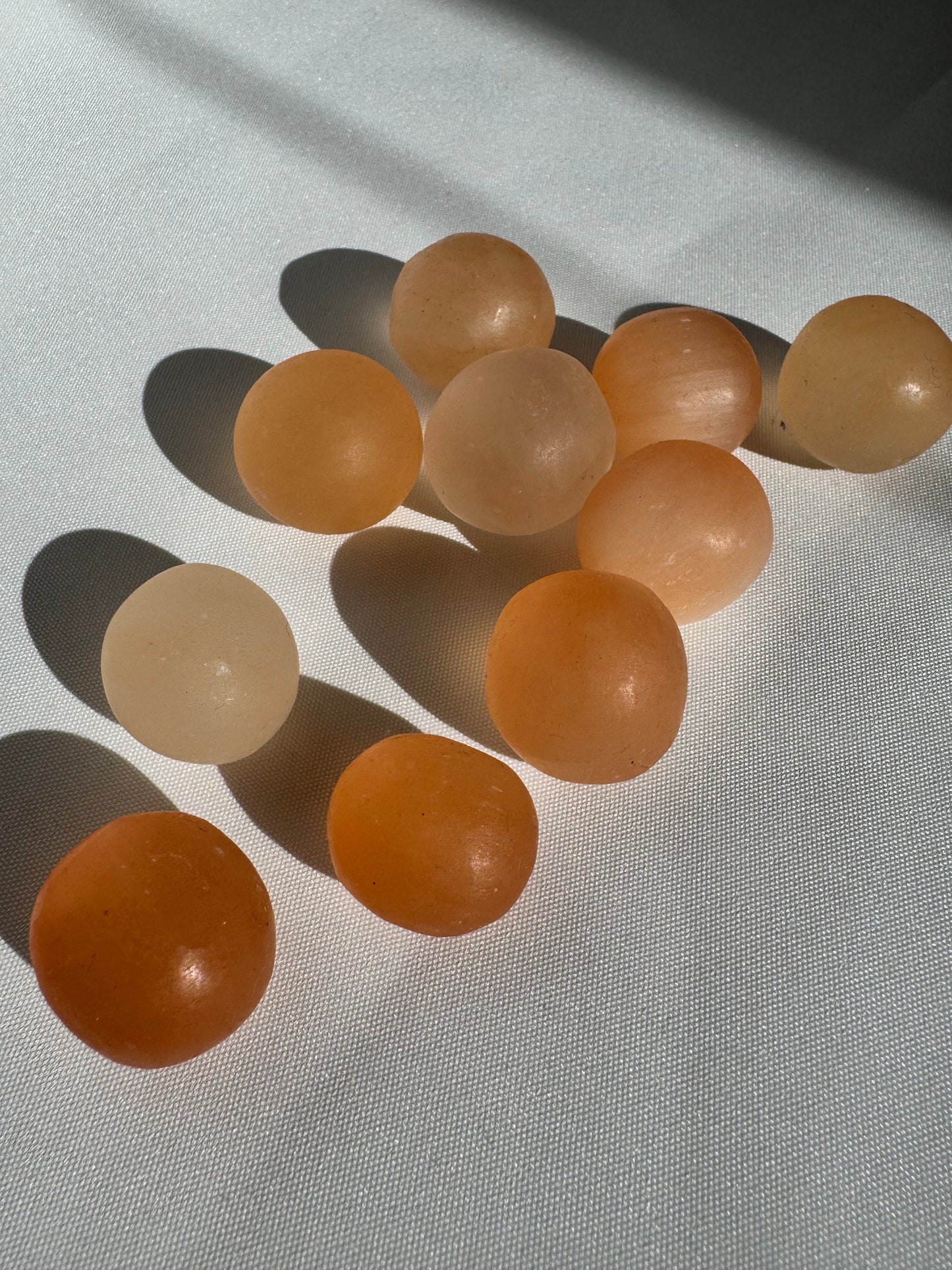 Orange Satin Spar Tumble Stones for emotional healing and chakra balance, displayed on white fabric under natural light.