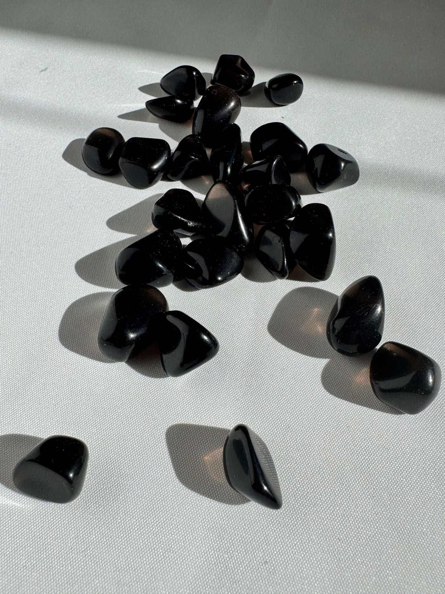 Collection of polished Apache Tears stones for grief support and energy cleansing, arranged on a white surface with soft sunlight reflections.