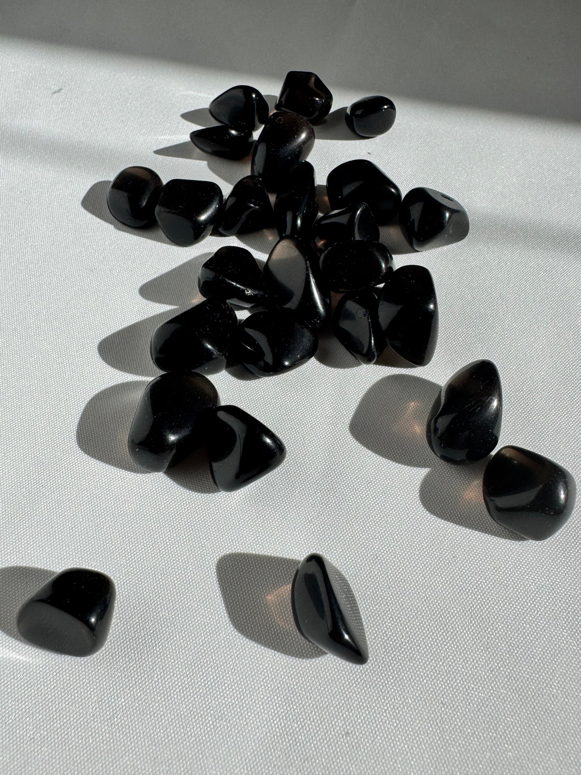 Collection of polished Apache Tears stones for grief support and energy cleansing, arranged on a white surface with soft sunlight reflections.
