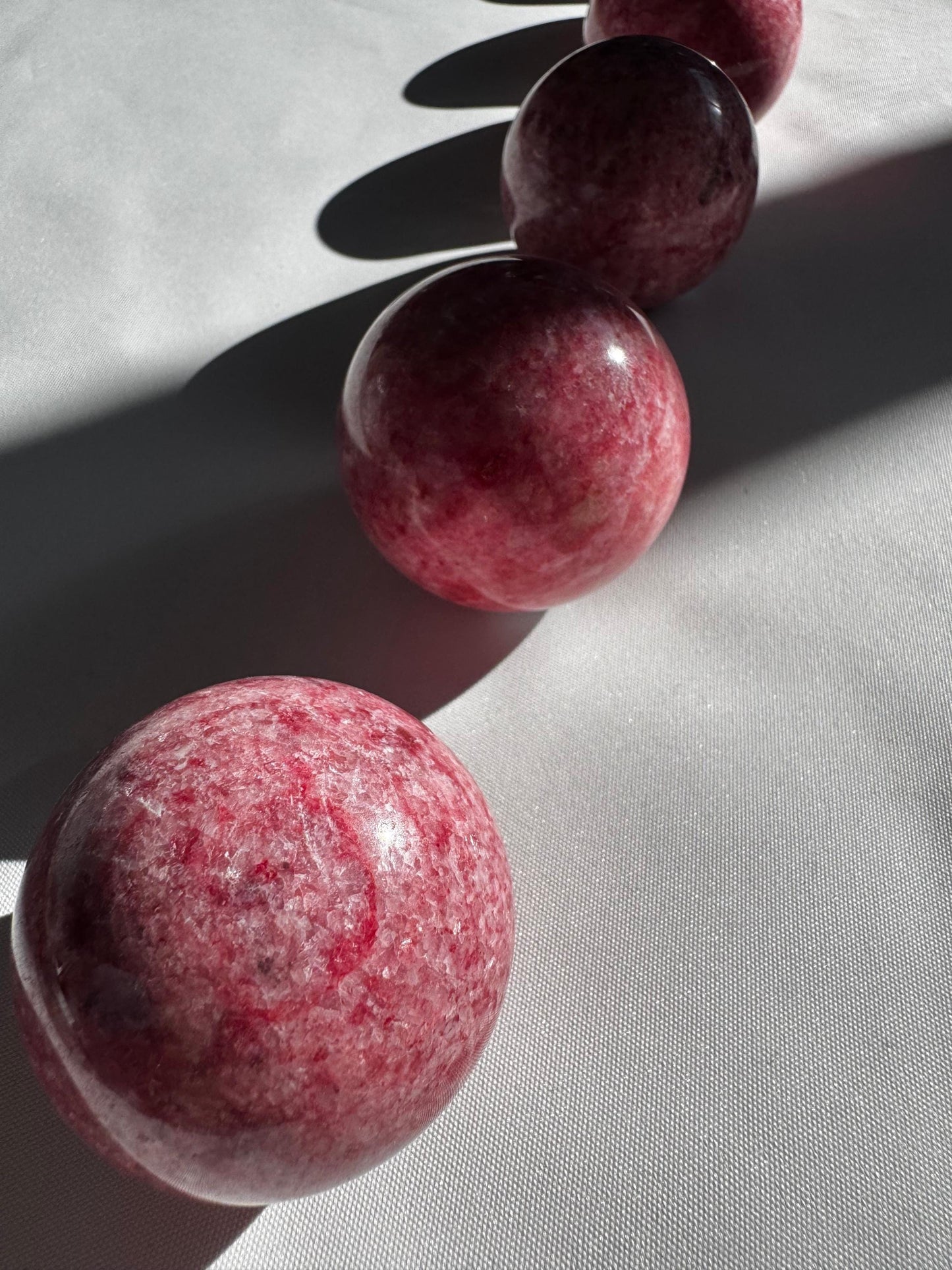 Set of four Pink Thulite Crystal Spheres arranged in a row on white fabric, showcasing their unique marbled textures and collectible quality.