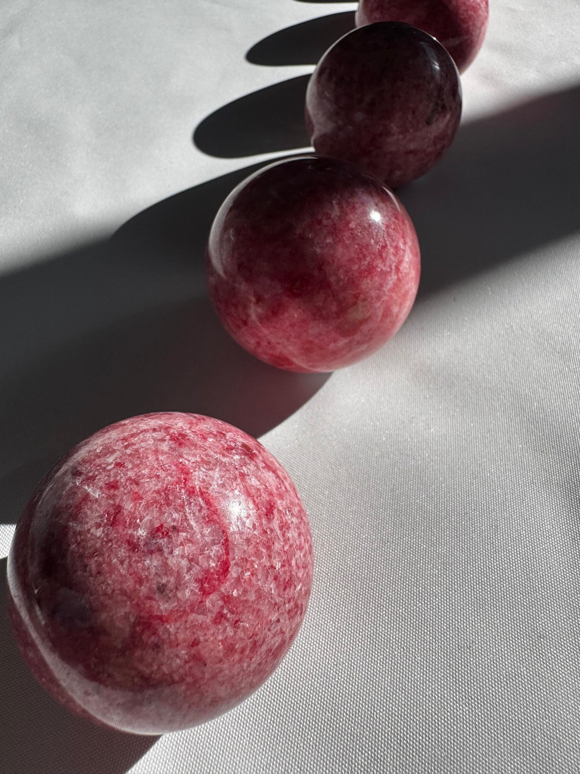 Set of four Pink Thulite Crystal Spheres arranged in a row on white fabric, showcasing their unique marbled textures and collectible quality.