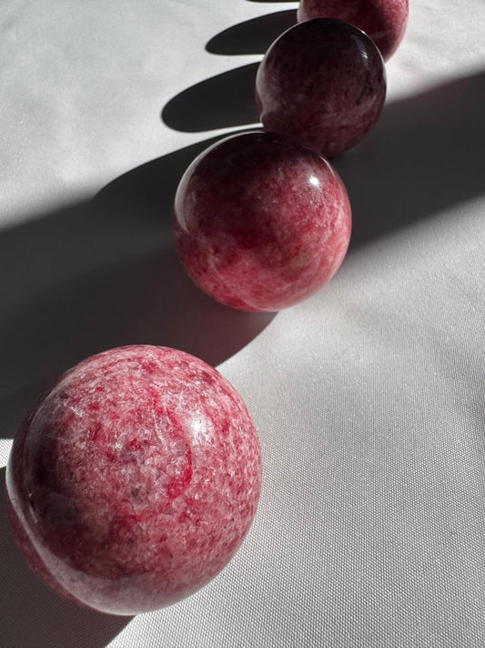 Set of four Pink Thulite Crystal Spheres arranged in a row on white fabric, showcasing their unique marbled textures and collectible quality.
