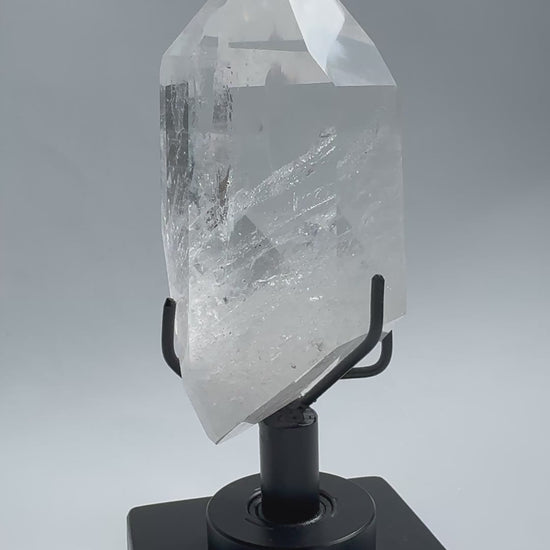 Clear Lemurian Quartz Crystal on sleek rotating base, showcasing natural striations and polished facets. A premium Quartz Crystal on Stand for collectors.