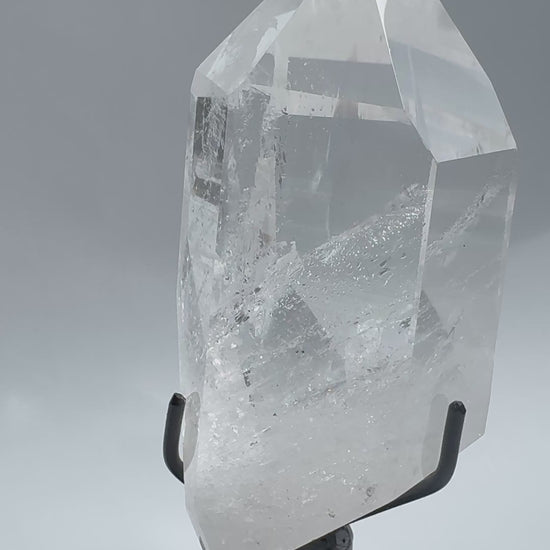 Lemurian Quartz Crystal with polished point and visible inclusions, mounted on a rotating black stand. A statement gemstone from Bahia, Brazil.